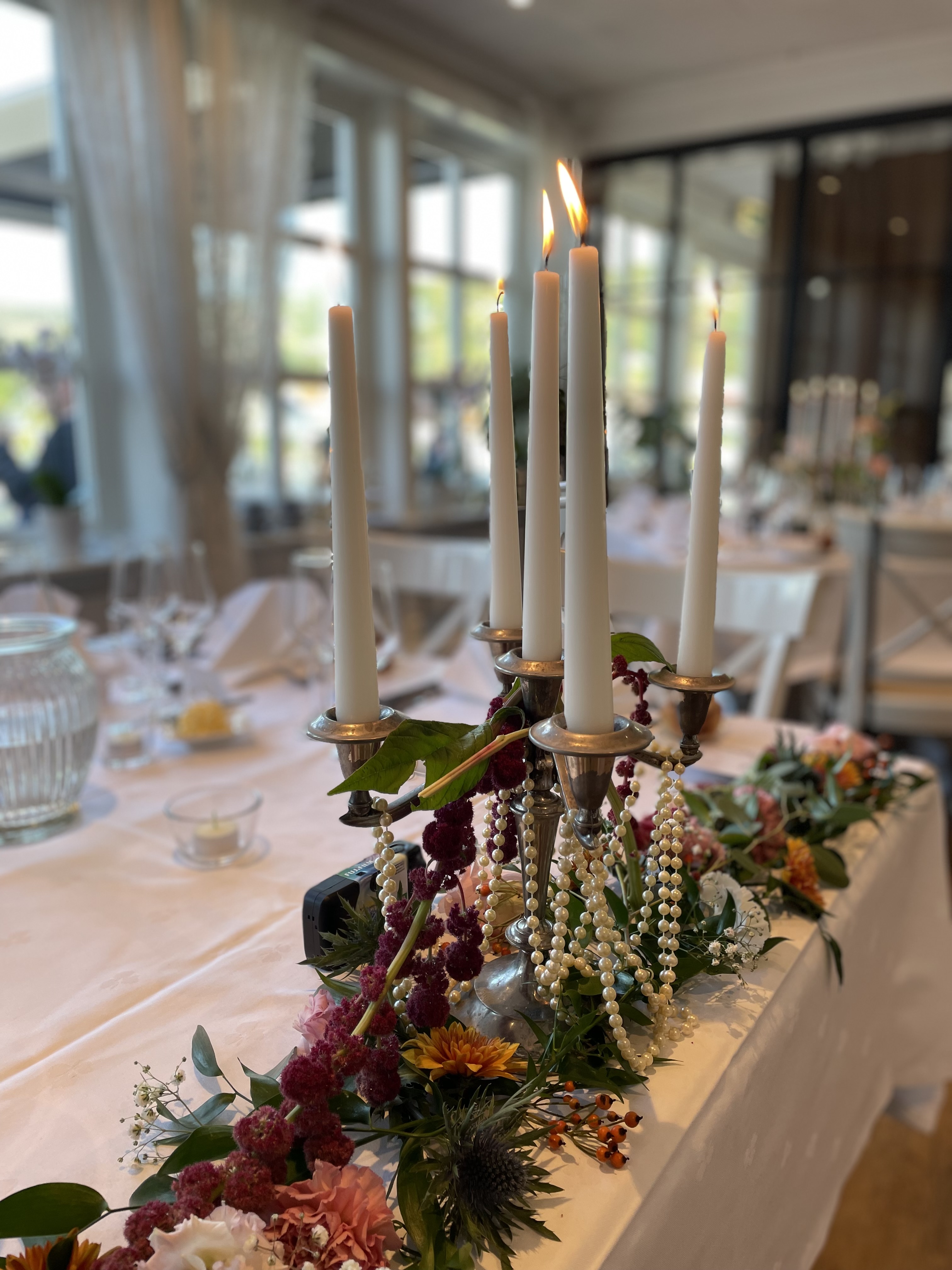 Detalj fra bord dekket med hvite servietter, høye glass og nydelige, hvite blomster