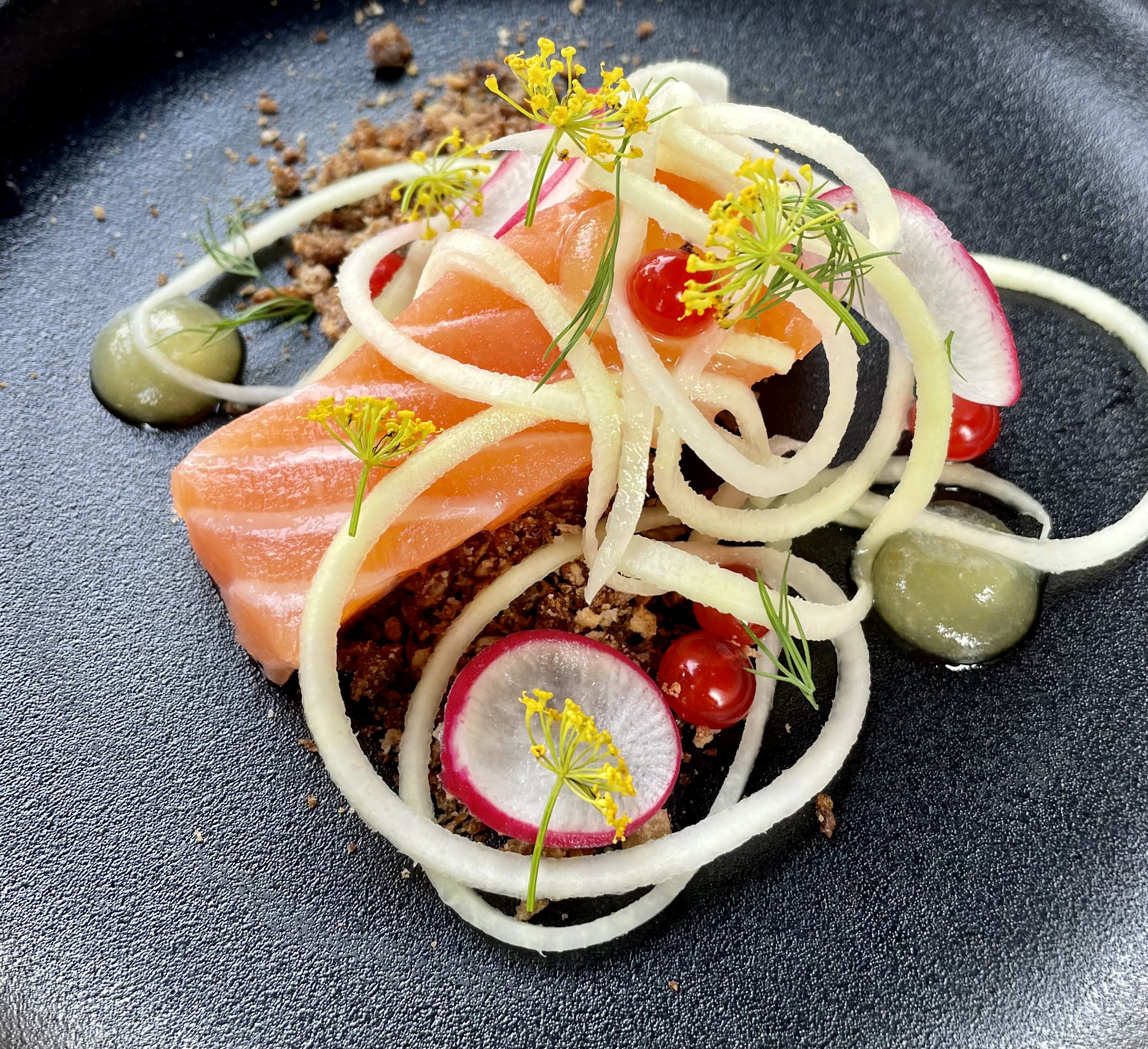 -En kokk heller saus over kjøtt og grønnsaker på en ferdig tilberedt rett med pommes frites i liten metallbøtte -