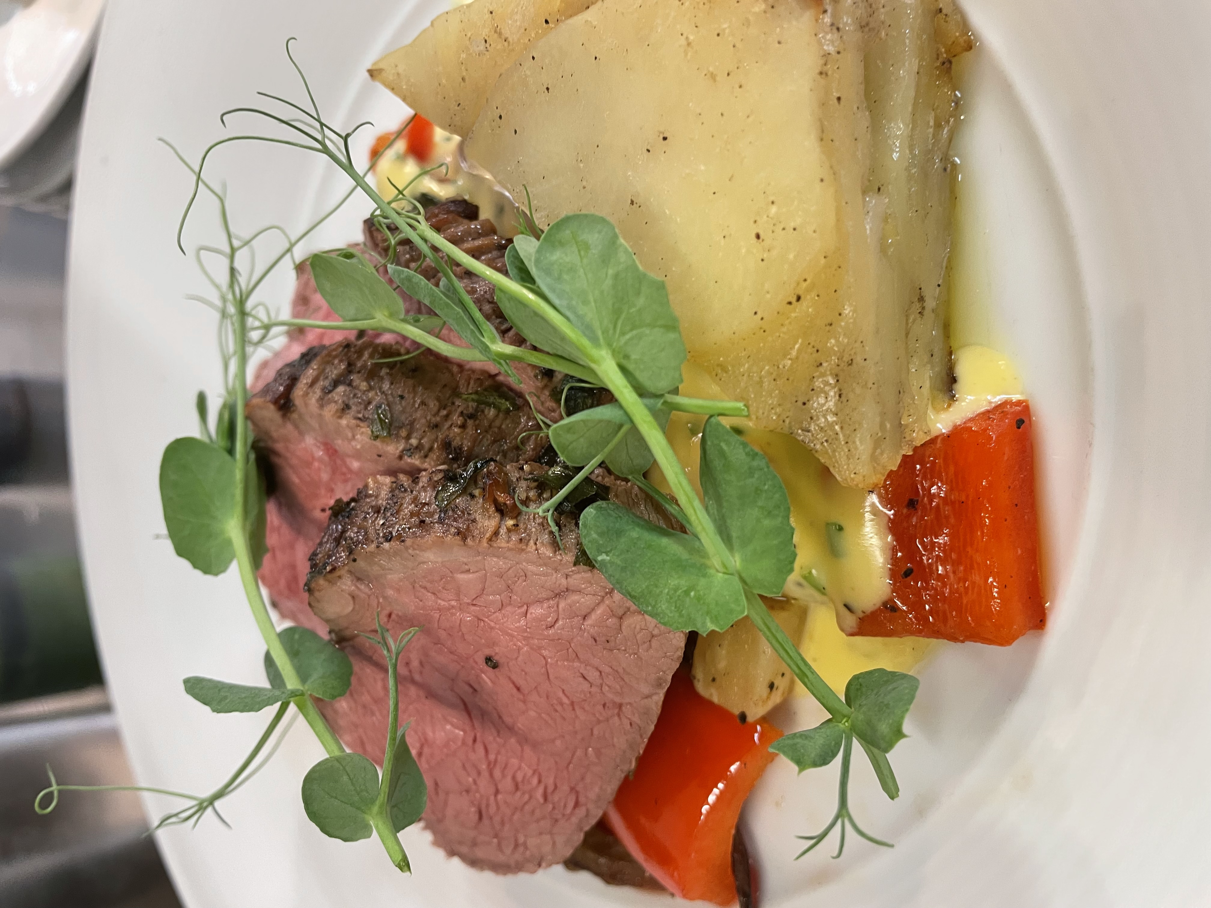 -En kokk heller saus over kjøtt og grønnsaker på en ferdig tilberedt rett med pommes frites i liten metallbøtte -