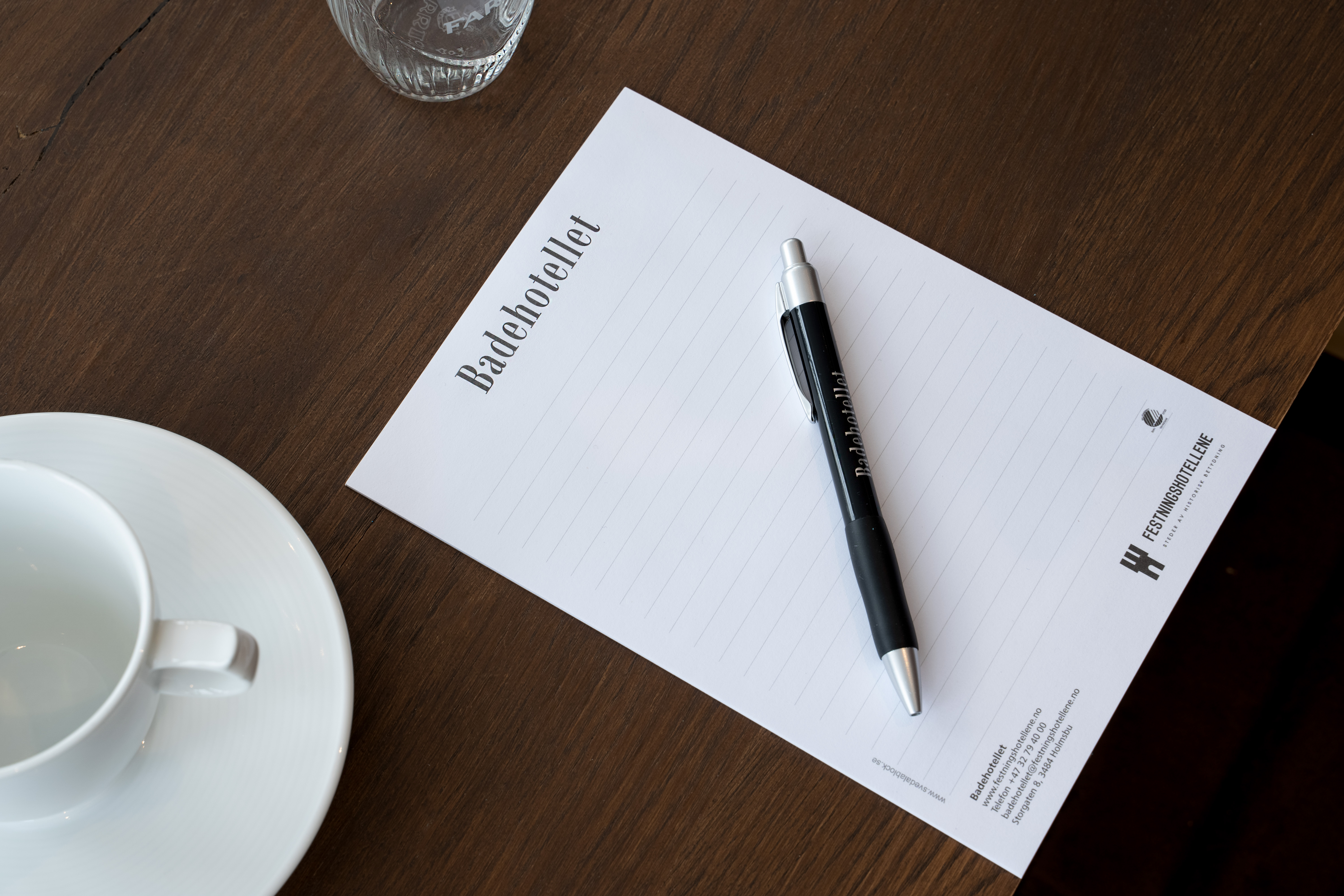 Notatblokk og penn merket med Badehotellet på konferansebord med kaffekopp